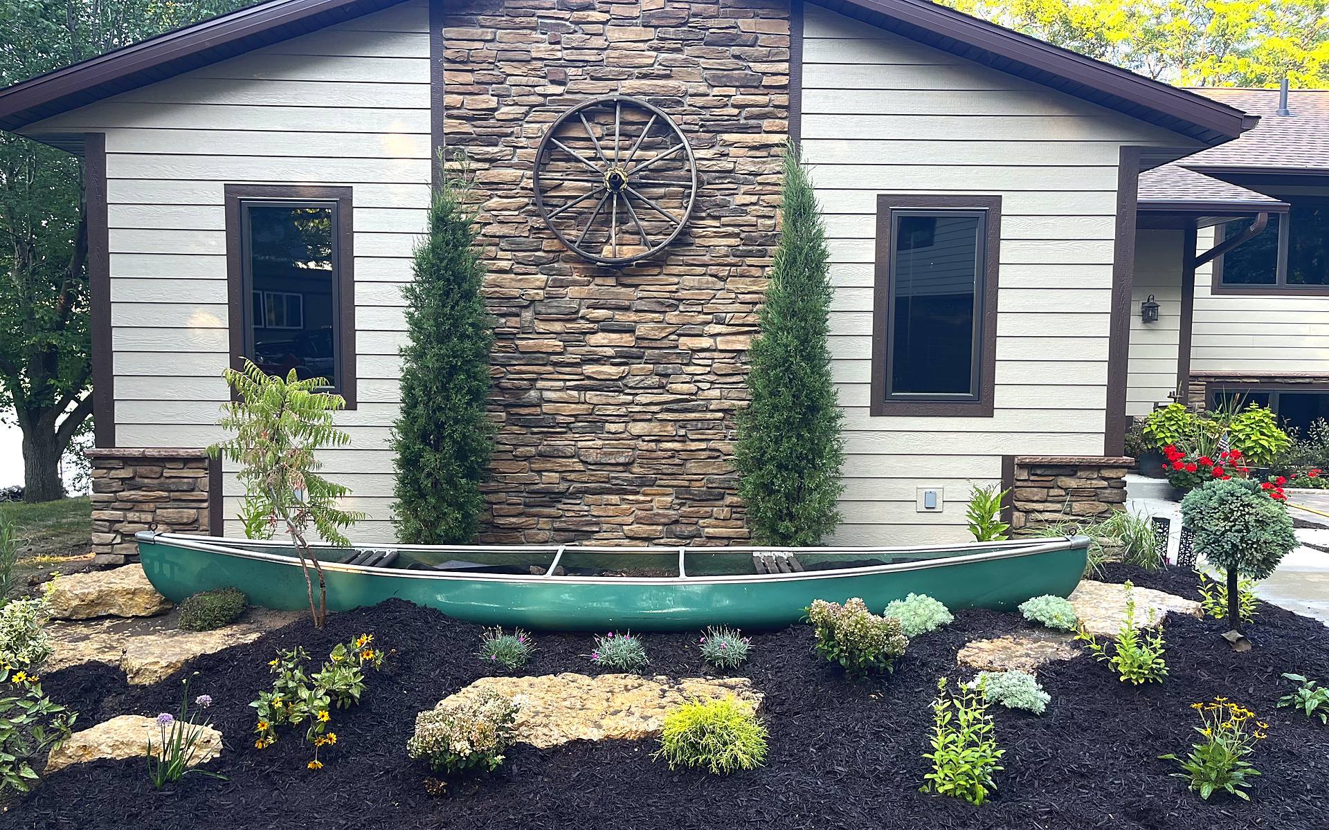 Canoe planter flower bed with limestone boulders and mulch beside a lake house, installed by New View Landscaping